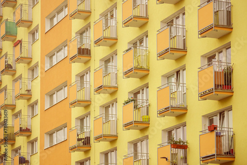 Żółto-pomarańczowa elewacja bloku mieszkalnego z wieloma balkonami. Styl lat siedemdziesiątych. 