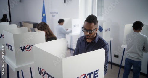 High angle of multiethnic European people voting at polling station during EU elections. Diverse voters fill out ballots in voting booths. Election Day in the European Union. Civic duty and democracy.