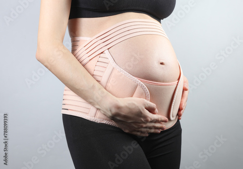 Young Pregnant woman with orthopedic belt for back and belly support. Bandage for pregnant women. Special belt for the 3rd trimester. Studio shot on a gray background