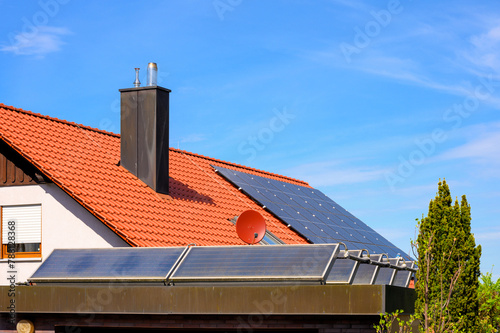 Solarthermieanlage auf Garagendach vor rotem Hausdach mit Photovoltaikanlage 