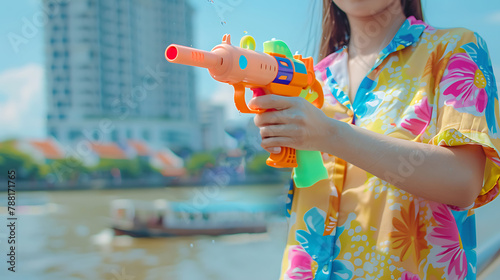 Summer fun: Woman holding colorful squirt water gun with city background, concept for Water festival holiday.