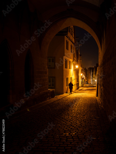 Person walking the streets of Rothenburg ob der Tauber at night, framed by an archway