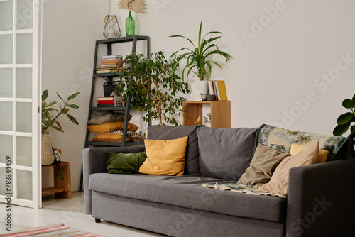 Part of spacious living room of modern apartment with comfortable couch with cushions surrounded by green domestic plants in flowerpots