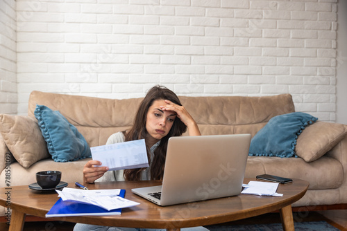 Young stressed woman having issue with utility bills expense, sitting at home trying to calculate and see bad finance bank report, searching for mistake. College student girl with money problem.