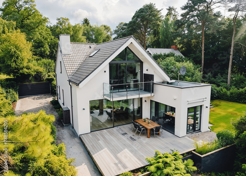 Luftaufnahme eines weißen Hauses mit grauem Dach, großen Fenstern und Terrasse im Garten