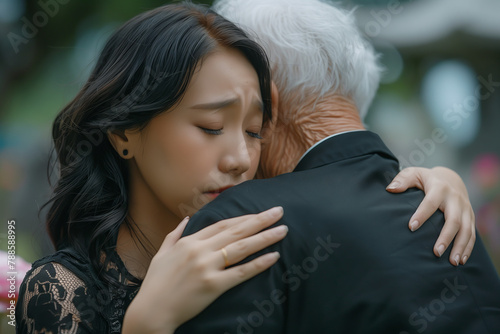 Embrace Across Generations in Grief. A young woman in a black dress tearfully embraces an elderly man in a moment of shared sorrow
