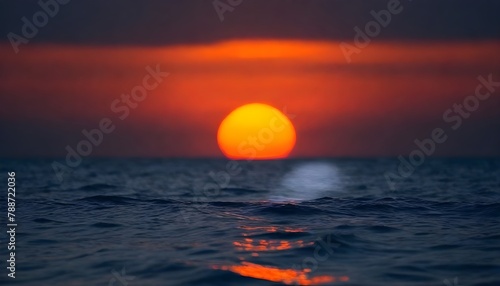 Out of focus sun setting over the ocean glowing orange with dark blue background