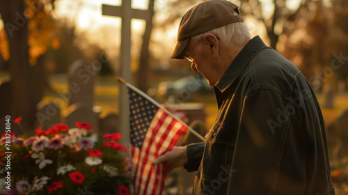 An elderly veteran standing solemnly by a decorated cross in a cemetery, his hand resting on the American flag, lost in silent remembrance.