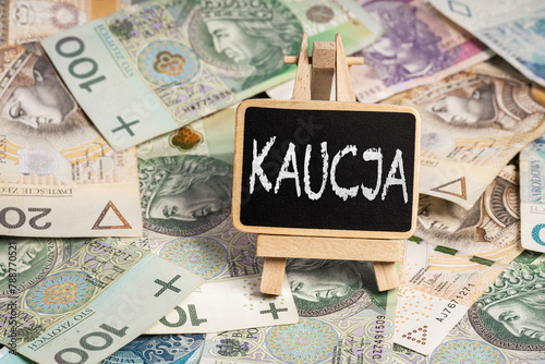 Black writing board on a wooden frame with the inscription "Kaucja", Polish zloty PLN banknotes scattered in the background (selective focus) translation: deposit