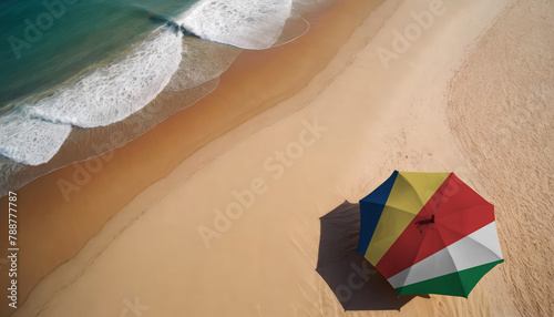 An aerial vista of a sandy beach with gentle ocean waves, featuring a beach umbrella adorned with the Seychelles flag. Ideal for Seychelles tourists seeking seaside relaxation