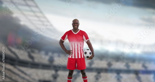 Man in red and white soccer uniform holding ball, standing on a field