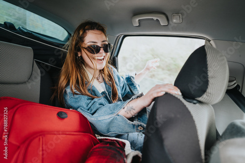 A cheerful young woman wearing sunglasses is laughing while sitting in the backseat of a car, signaling a sense of adventure and freedom.