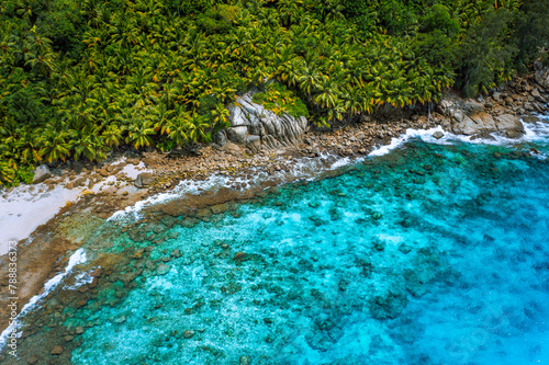 Aerial view of wild secluded lonely beach with rough granite rocks, white sand, palm trees in a jungle and turquoise water of the indian ocean at police bay on the seychelles