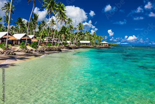 Tropical beach with with coconut palm trees and villas on Samoa