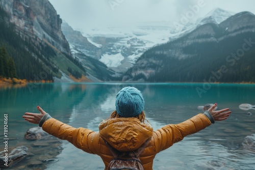 With open arms, a person embraces the breathtaking view of a snow-laden mountainous landscape reflecting in a lake