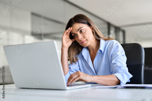Worried fatigued mature business woman having headache at work. Tired upset busy 40s middle aged businesswoman feeling stress having problem at workplace looking at laptop computer in office.