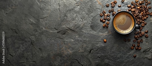Image of a cup of coffee and coffee beans on a dark stone background, displayed horizontally with empty space for text, as seen from the top.