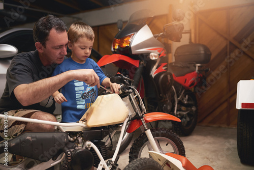 Parent, son and fixing with bike in garage at home for teamwork, support and repair with tools. Family, father and child for bonding, helping and together as mechanic for motorbike in carport