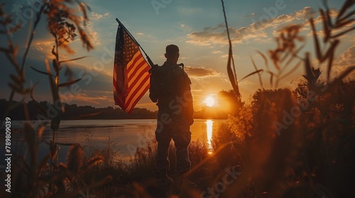 A soldier stands holding an American flag at sunset.
