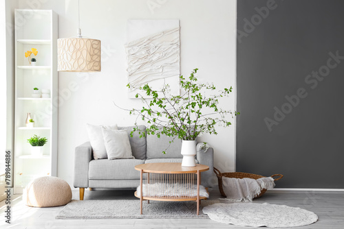 Comfortable sofa and vase with blooming branches on coffee table in living room