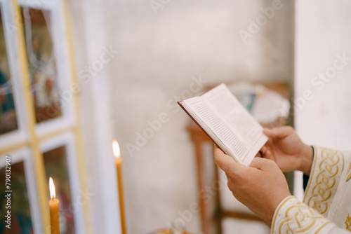 Priest reads the bible near the table with lit candles in the church. Cropped. Faceless