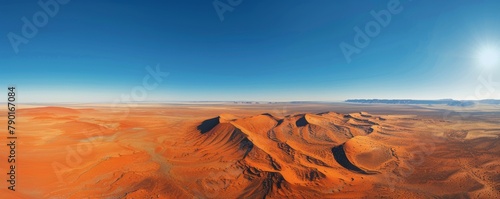 Aerial view of red desert sands contrasted against a clear blue sky.