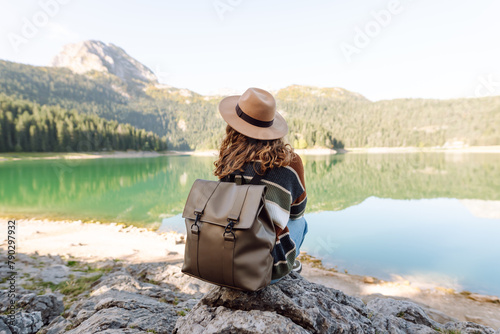 Back view young woman with backpack loking the view of the mountain lake in sunny weather. The concept of travel, vacation. Active lifestyle.