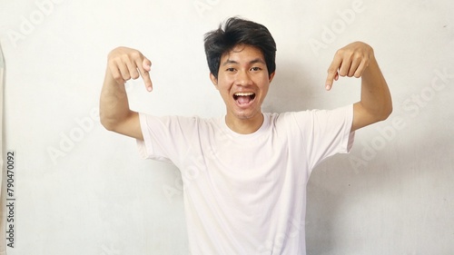young asian man posing happily while pointing down on a white background