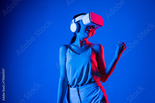 Smart female standing wearing VR headset connecting metaverse, future cyberspace community technology. Woman victory competition. Lady gesticulate raising arm slightly with happy face. Hallucination.