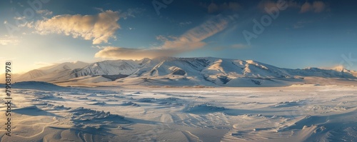 A panoramic vista of a snow-covered mountain range bathed in the golden light of the setting sun, casting long shadows across the landscape.