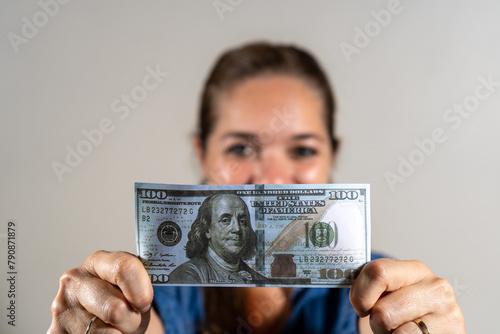 Mujer contenta mostrando a cámara un billete de 100 dolares
