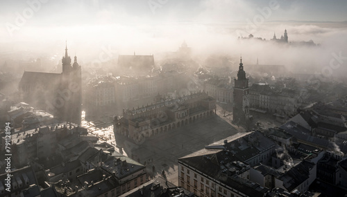 Soft lighted Main Square in Krakow (view of Saint Mary Basilica - Mariacki Church, cloth hall - Sukiennice, town hall and Wawel castle) during beautiful, foggy sunrise, Poland