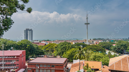 Panorama of the modern city. Multi-storey buildings, skyscrapers among lush green tropical vegetation. A tall TV tower against a blue sky and clouds. The ocean is far away. Malaysia. Malacca