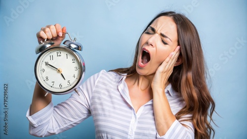 An exhausted woman holds an alarm clock and stifles a yawn.