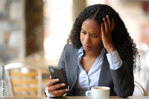 Worried businesswoman checking smart phone in a bar terrace