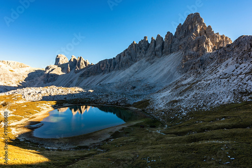 Photo of the Monte Paterno (Paternkofel) over the lake Laghi dei Piani with a reflection in the clear calm water surface during an early autumn sunny day with blue sky