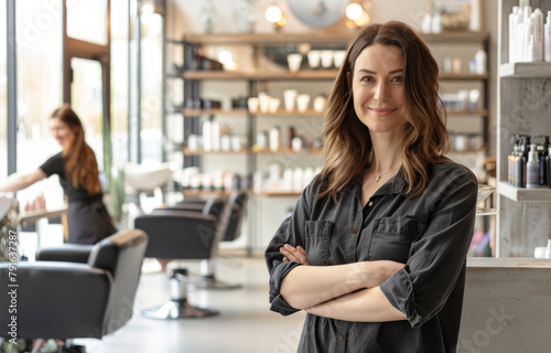 A photo of beautiful salon owner standing with her arms crossed in front, wearing an apron and smiling at the camera while other stylist works on hair