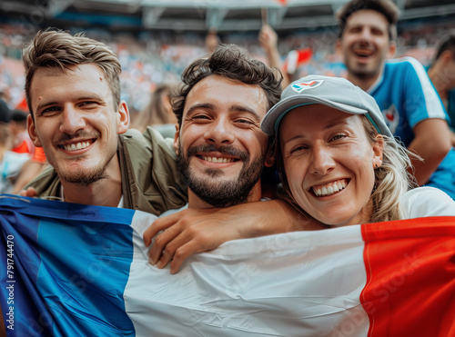  amigos franceses sosteniendo una bandera de España animando a su equipo, contentos sonriendo a cámara, con fondo de estadio olimpico deportivo con multitud de gente