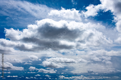 Cloudscape on a sunny day with white and gray cloud formations, hidden sun and blue sky. Wide angle shot on a day with nice weather. 