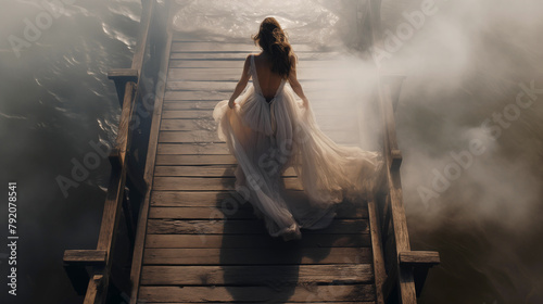 Silhouette of a woman walking on a pier, wearing a white vintage dress, heading towards the water, with the sun shining through the fog. High angle shot.