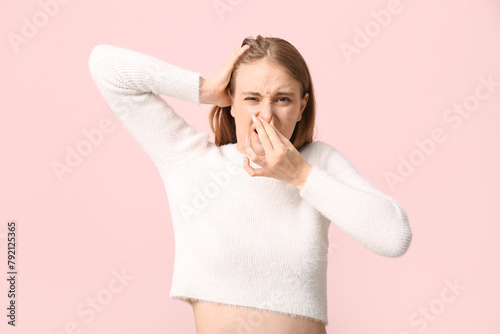 Young woman feeling disgusting smell on pink background