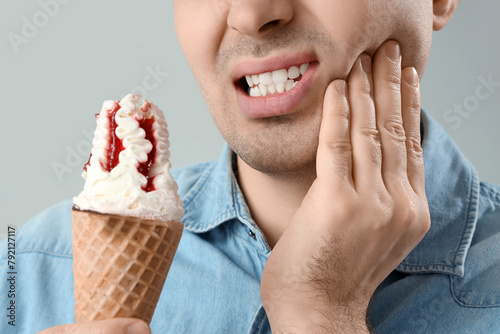 Young man with ice cream suffering from toothache on light background, closeup