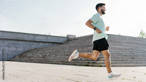 A bearded runner with a focused gaze propels forward in a dynamic stride along a vast urban staircase, under the open sky.