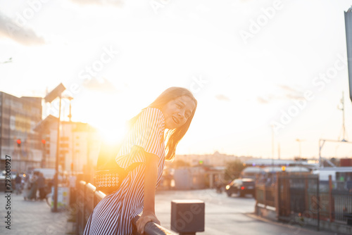 A beautiful teenage girl walks around the city against the background of sunlight, the model wearing the stripped dress and smiles with braces and backpack