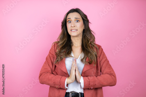 Young beautiful woman wearing casual jacket over isolated pink background begging and praying with hands together with hope expression on face very emotional and worried