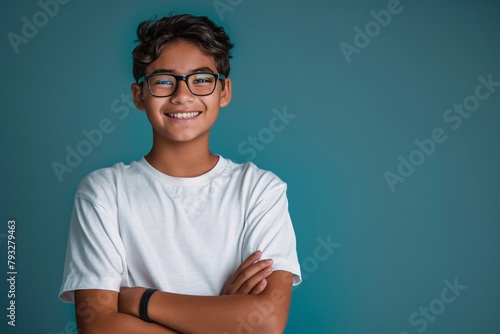 Portrait of a smiling teenage boy wearing eyeglasses, arms crossed, isolated on a blue background