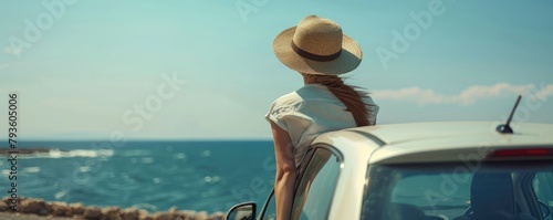 Rear view of a young woman in a hat, leaning on a vintage car looking out to the blue ocean. copy space for text.