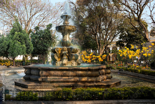 Park water fountain surrounded by trees and flowers.