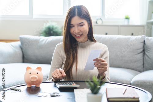 Happy asian young business woman, employee using calculator to calculate expenses of monthly, hand holding bills and receipt for to payment on table at home. Financial, finance of banking concept.