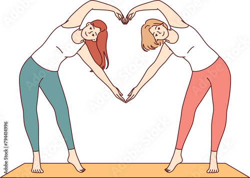 Paired yoga of two women doing aerobics or pilates standing on sports mat and making heart sign from hands. Attractive girls are interested in fitness and pilates to avoid excess weight